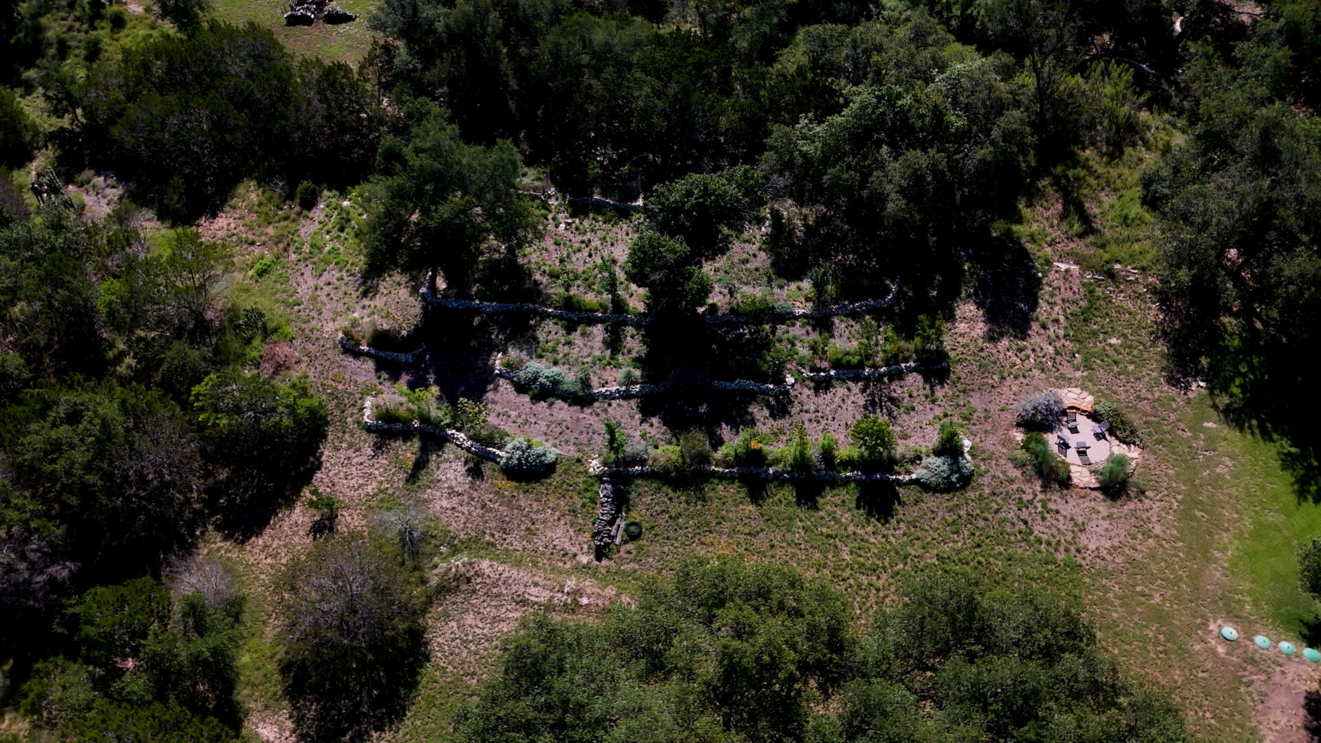 Overhead drone image of multiple dry stack limestone retaining walls forming terraces across a Central Texas hillside landscape.