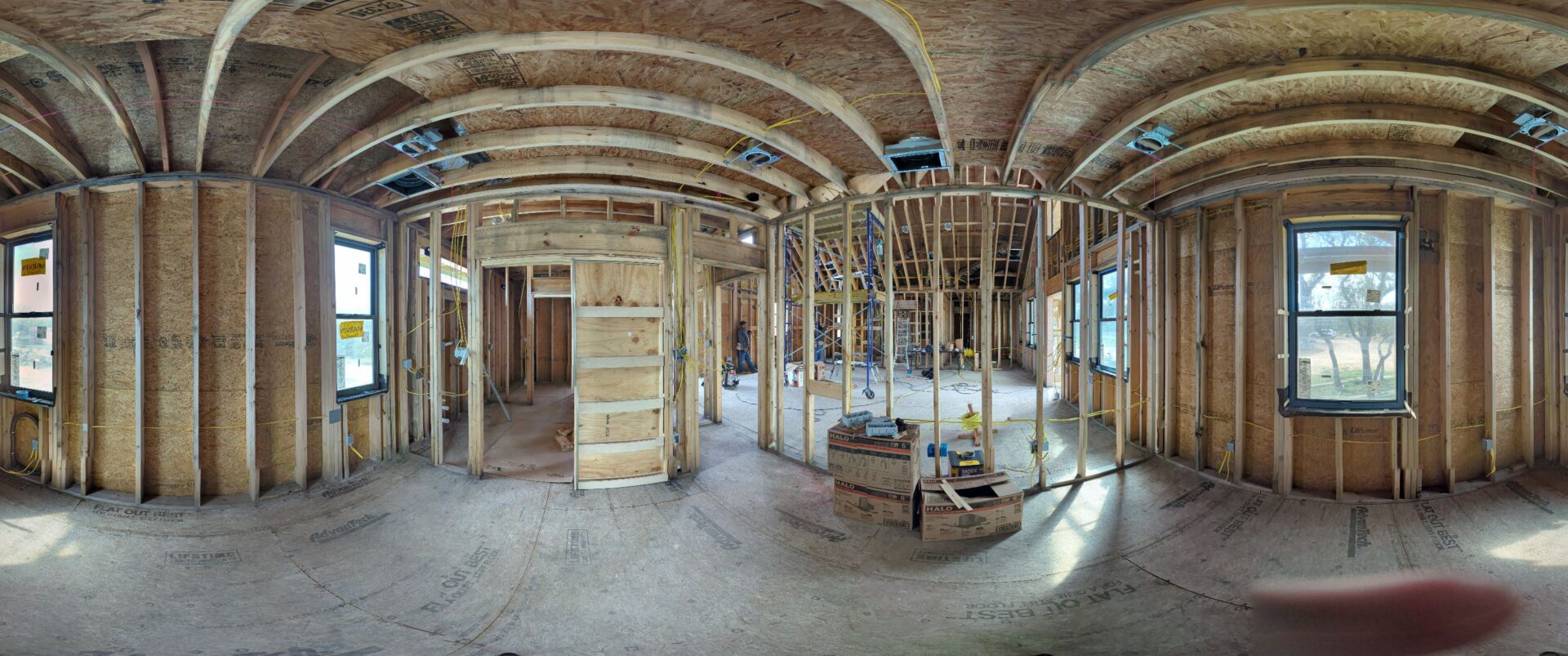 Panoramic view of two ecological homes under construction on a Central Texas property, sited among existing oaks.