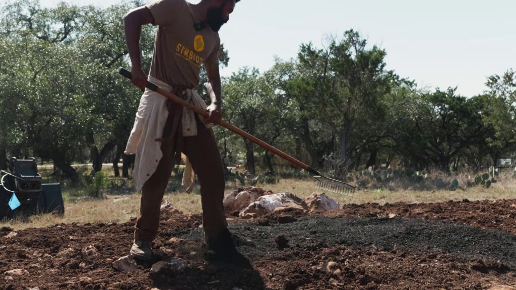 Crew member raking biochar into the topsoil of a planting berm in the Texas Hill Country