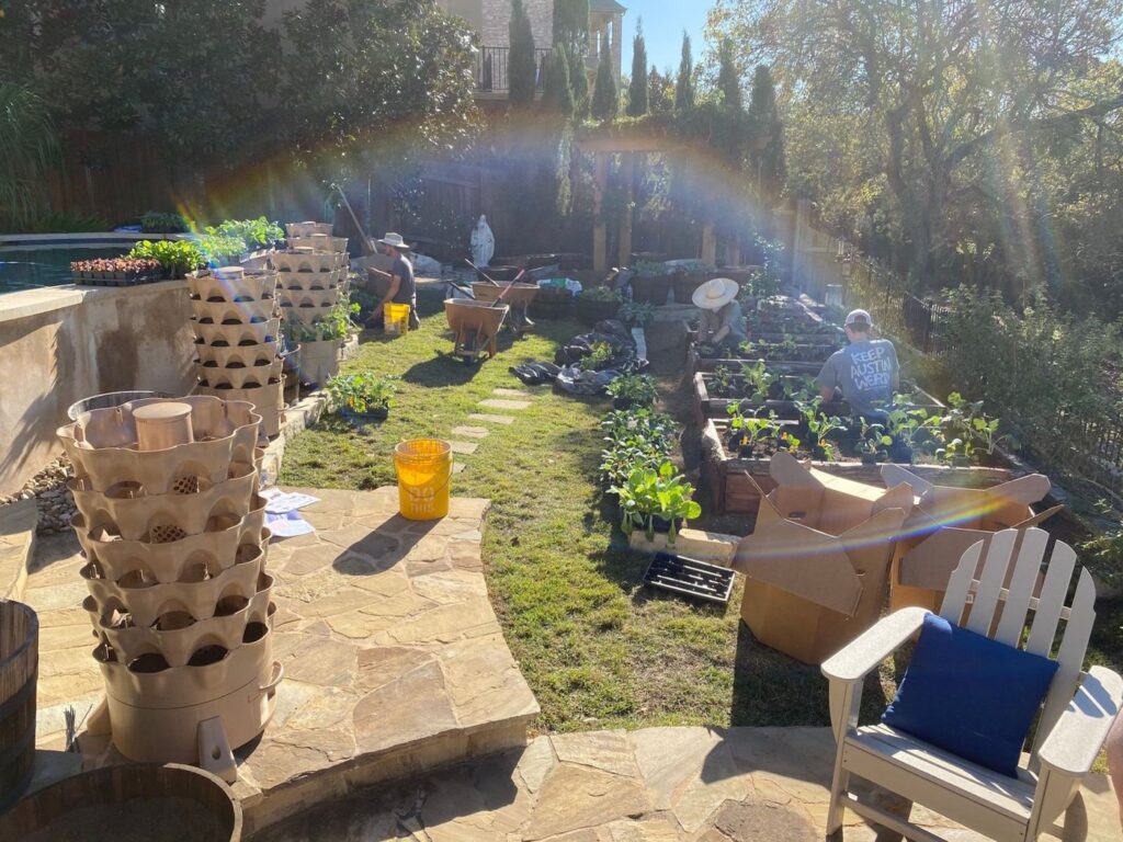 Symbiosis crew planting a raised-bed vegetable garden in an Austin backyard, with vertical planters and seedlings staged on the patio
